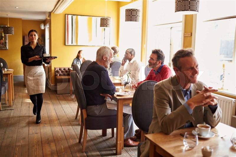 Customers at tables and waitress in busy restaurant interior, stock photo