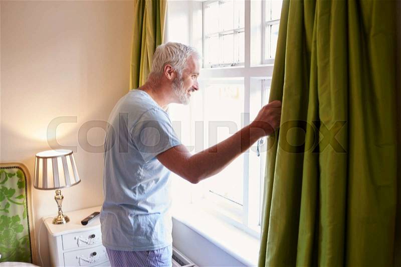 Middle aged man gets up and opens the curtains in hotel room, stock photo