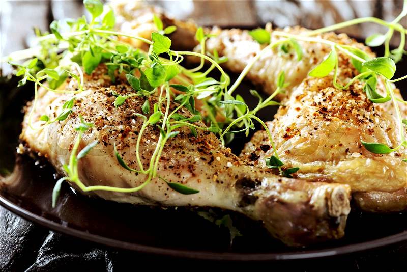 Grilled spicy chicken legs with herbs and spices on a black plate, stock photo