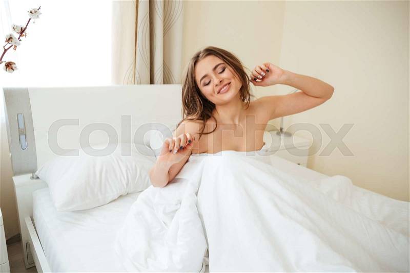 Happy woman stretching hands in the bed at home, stock photo