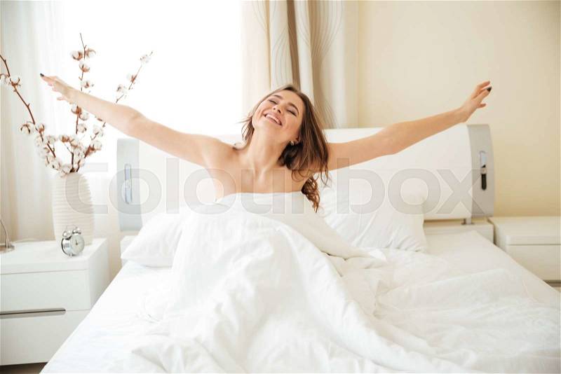Happy woman stretching hands on the bed at home, stock photo