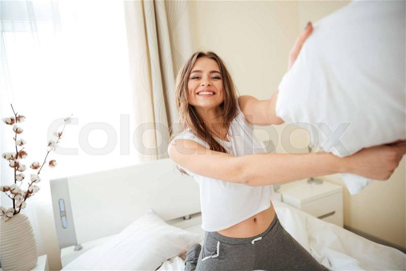 Smiling woman on the bed fighting with pillow at home, stock photo