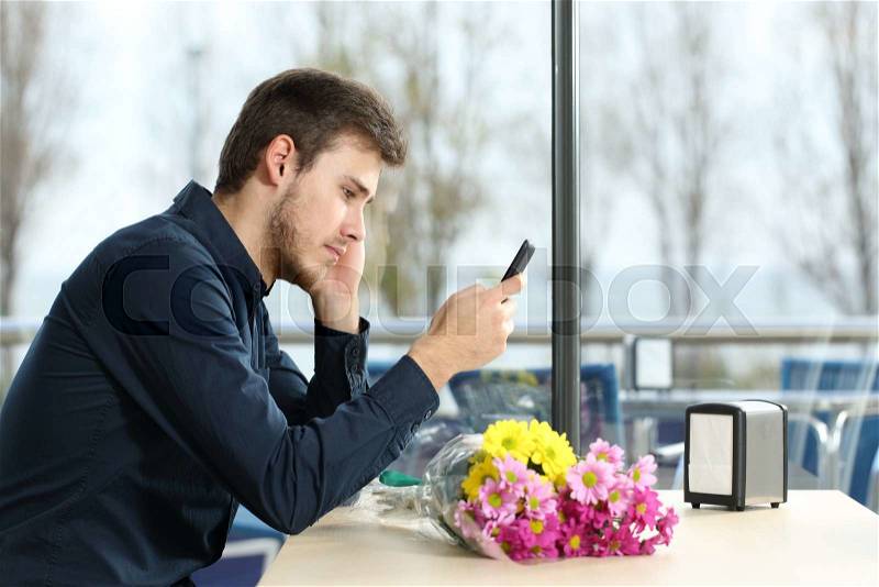 Sad man with a bouquet of flowers stood up in a date checking phone messages in a coffee shop, stock photo