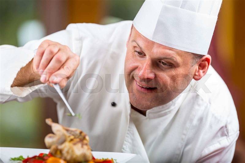 Chef. Chef cooking.Chef decorating dish. Chef preparing a meal. Chef in hotel or restaurant kitchen prepares decorating dish with tweezers. Chef cooking, only hands. Decorating grilled quail, stock photo