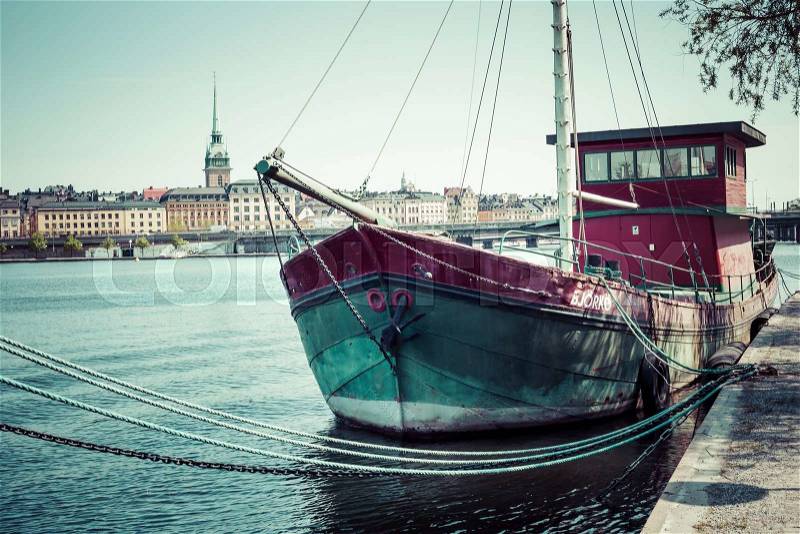 Old city buildings and old boats on water under blue sky in Stockholm, Sweden, stock photo