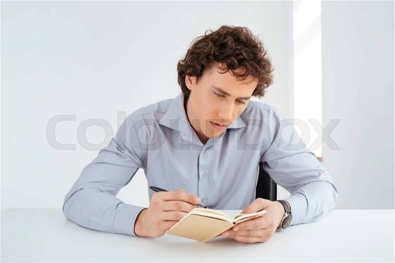 Young businessman writing notes in notebook in office, stock photo