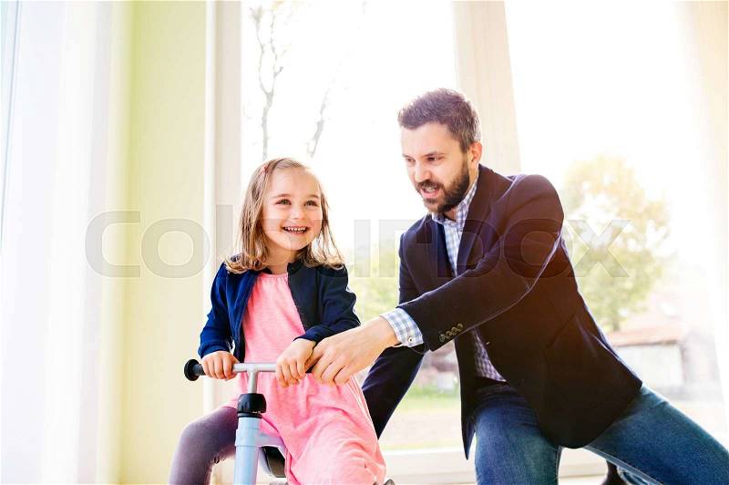 Father and daughter playing together, riding a bike indoors, sunny day, stock photo