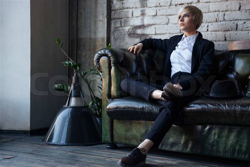 Stylish blonde girl sitting on the leather couch and thinking about something, stock photo