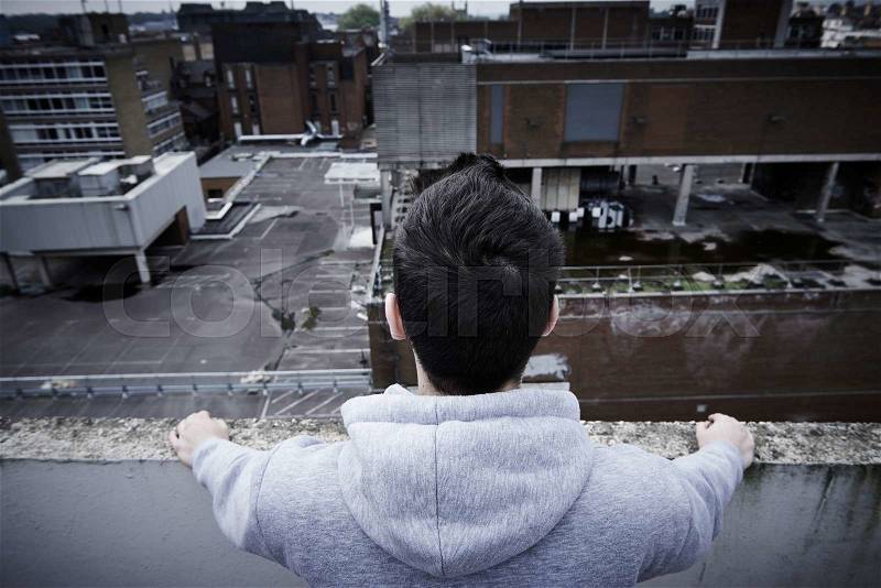 Depressed Young Man Contemplating Suicide On Top Of Tall Building, stock photo