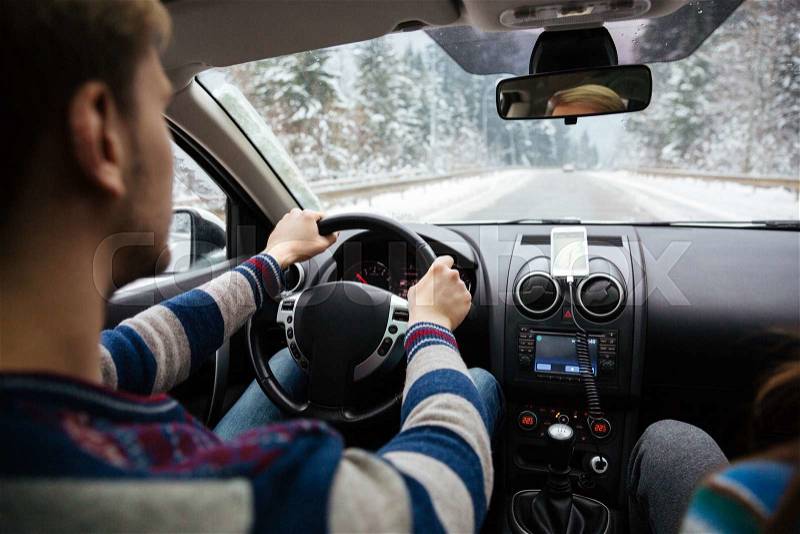 Back view of handsome young driver in stripes sweater driving through winter forest, stock photo
