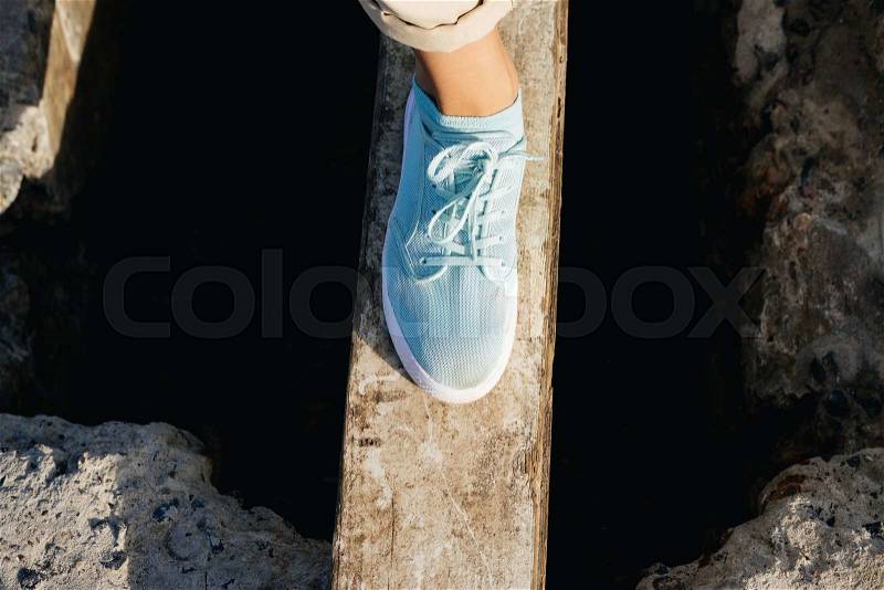 Female legs in beige pants and sneakers are on the board over the cliff, stock photo