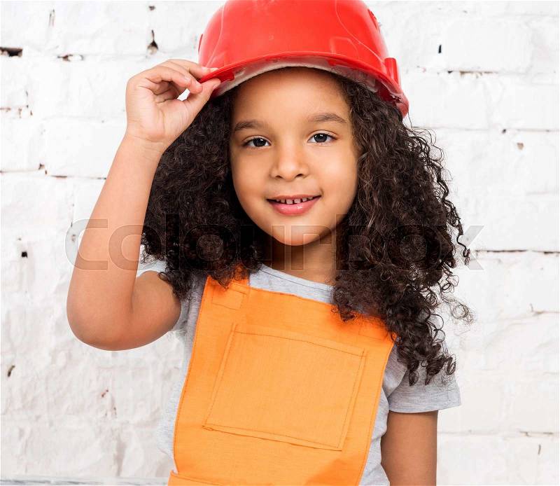 Cute little girl in orange repairmen uniform and helmet, stock photo