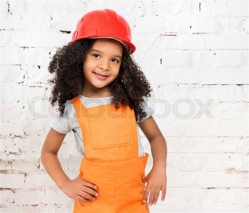 Cute little girl in orange repairmen uniform and helmet, stock photo