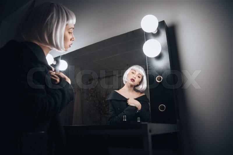 Attractive young woman in blonde wig sitting in front of the mirror in dressing room, stock photo