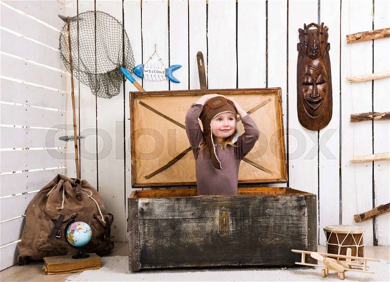 Funny little girl-pilot in old wooden chest with hands up, stock photo