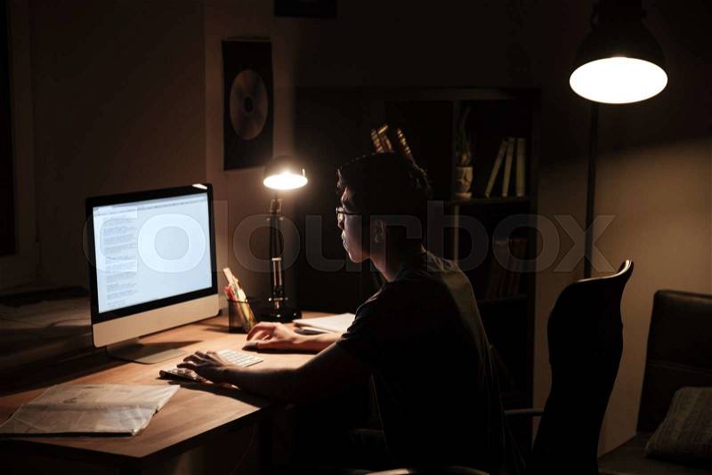 Focused man sitting and using computer in dark room, stock photo