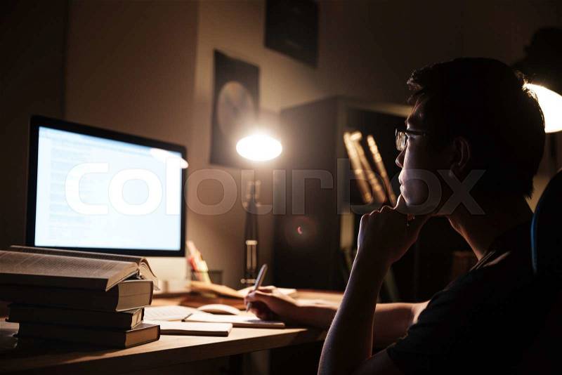 Pensive man writing and working with computer in dark room, stock photo