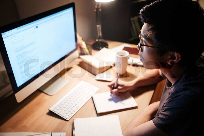 Man reading and writing using information from computer, stock photo