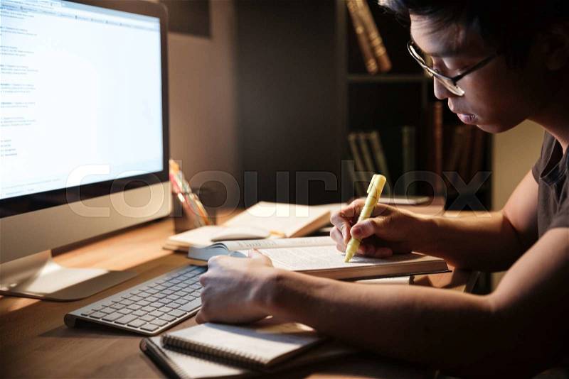 Serious asian young man studying with books and computer in dark room at home , stock photo