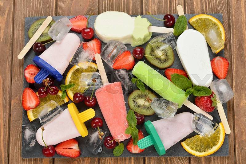 Ice cream, popsicles, ice and various fruits on a black plate, stock photo