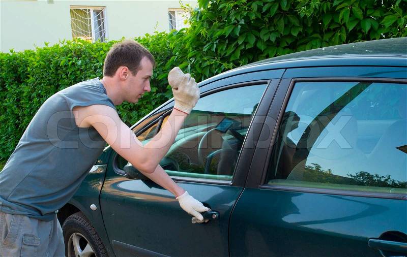 The man breaks a window of the car a stone, stock photo