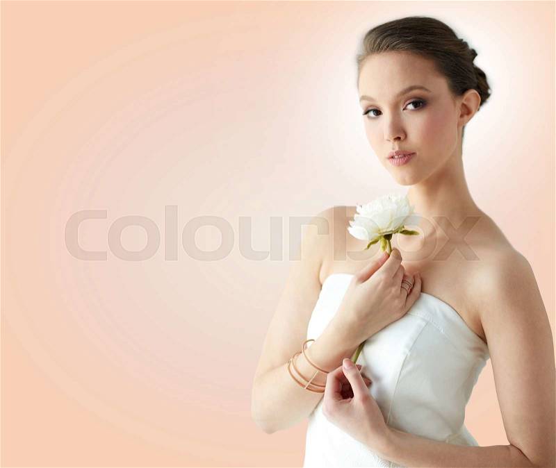 Beauty, jewelry, people and luxury concept - beautiful asian woman or bride in white dress with peony flower, golden ring and bracelet over beige background, stock photo