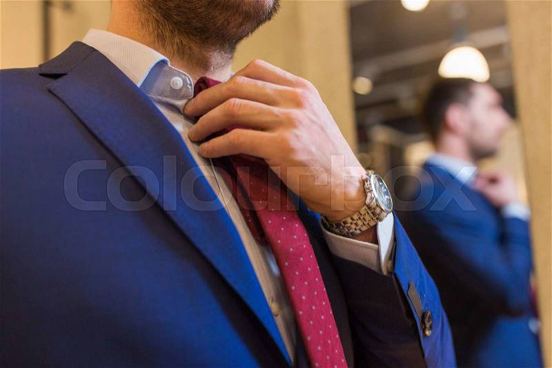 Sale, shopping, fashion, style and people concept - elegant young man choosing and trying tie on at clothing store, stock photo