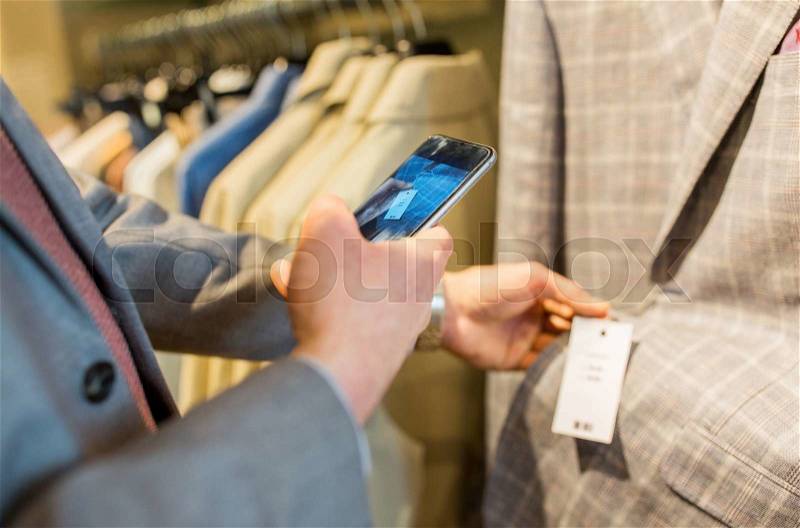 Sale, shopping, fashion, technology and people concept - close up of man in suit with smartphone choosing clothes at clothing store, stock photo