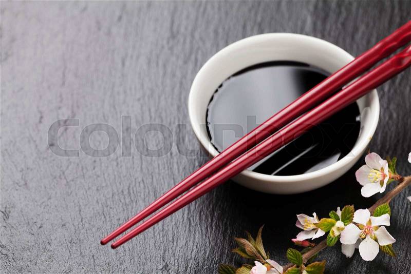 Japanese sushi chopsticks, soy sauce bowl and sakura blossom on black stone background. Top view with copy space, stock photo