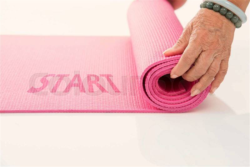 Senior hand\'s rolling pink yoga mat on white with message start, stock photo