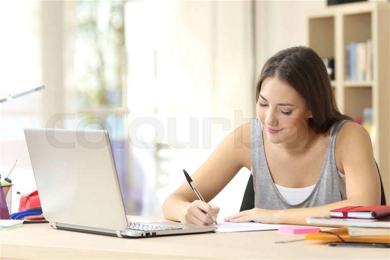 Beautiful student studying on line and learning writing notes in a desk at home, stock photo