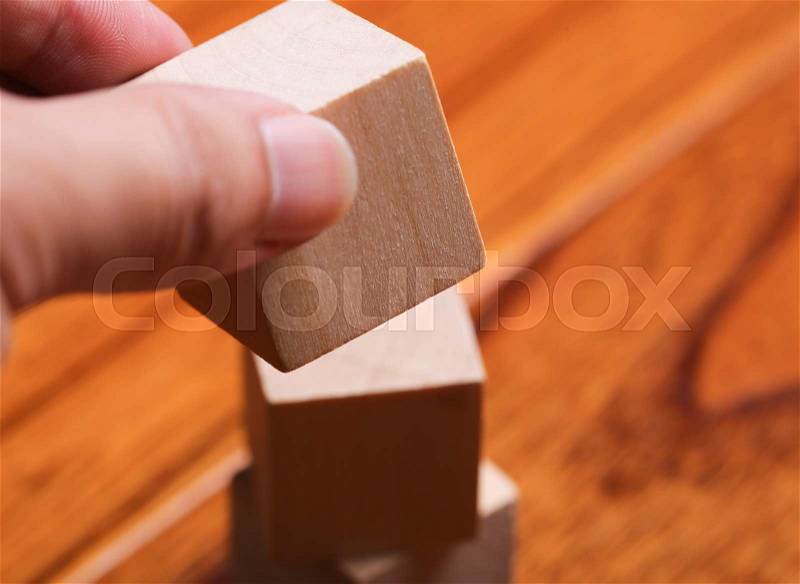 Hand is putting the block onto the block tower with wooden floor background, stock photo