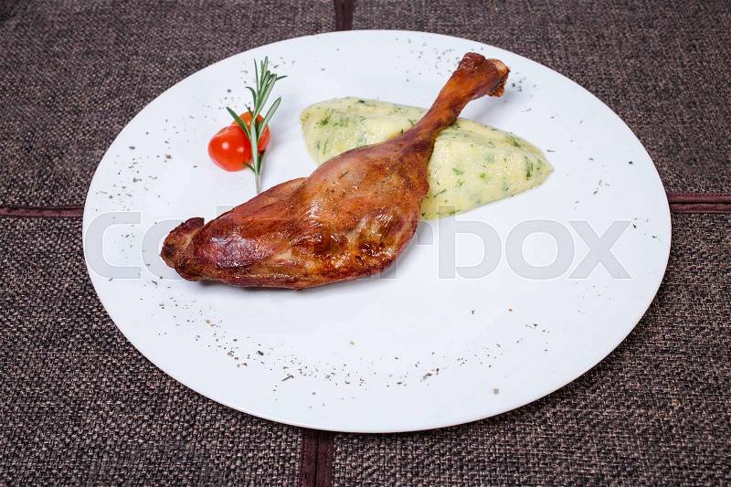 Delicious duck leg confit with delicate potato puree and posemary. Plate located on a brown tablecloth background, stock photo