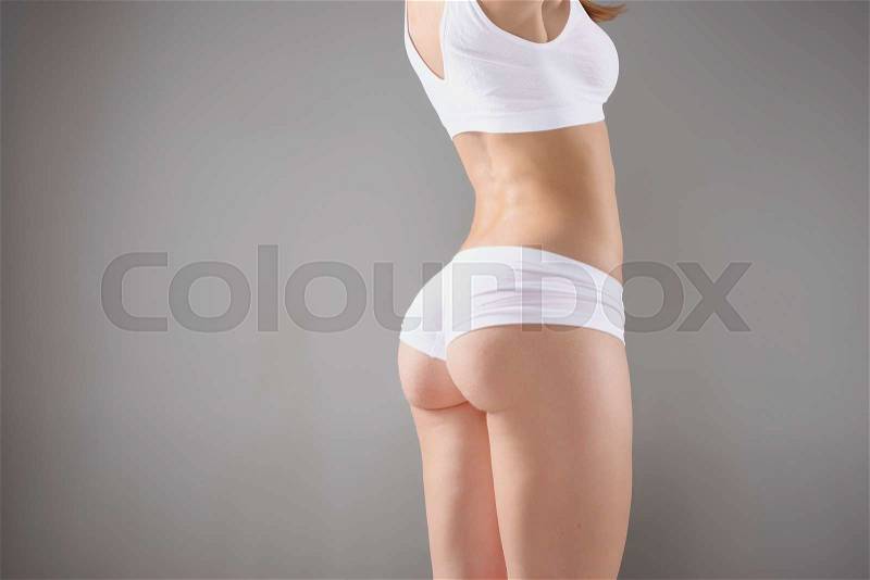 Young, slim, healthy and beautiful woman in white lingerie on the gray background, stock photo