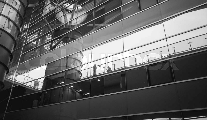 Black and white image of people reflecting in modern glass building, stock photo