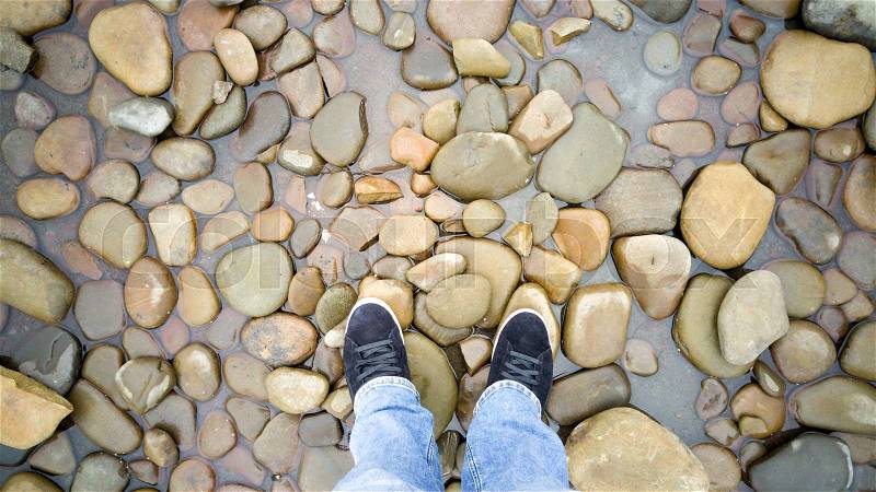 Toned photo of male feet in sneakers standing on pebbles in sea, stock photo