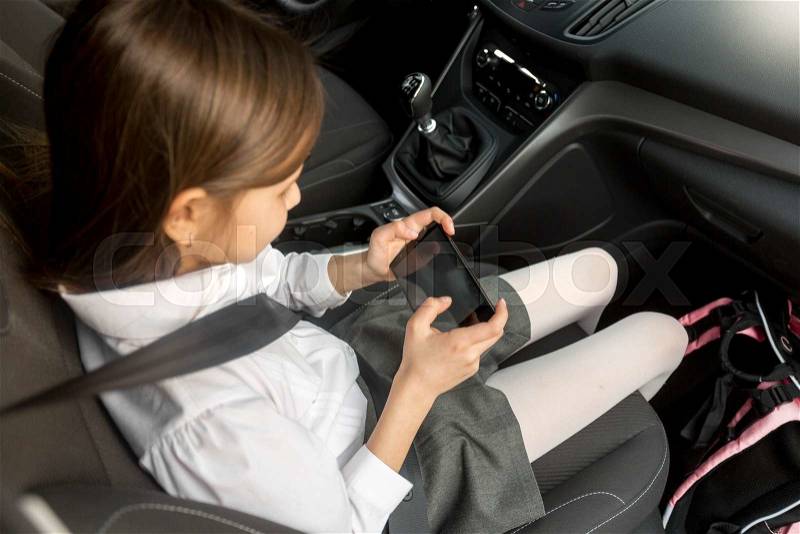 Cute little girl using smartphone while going to school by car, stock photo