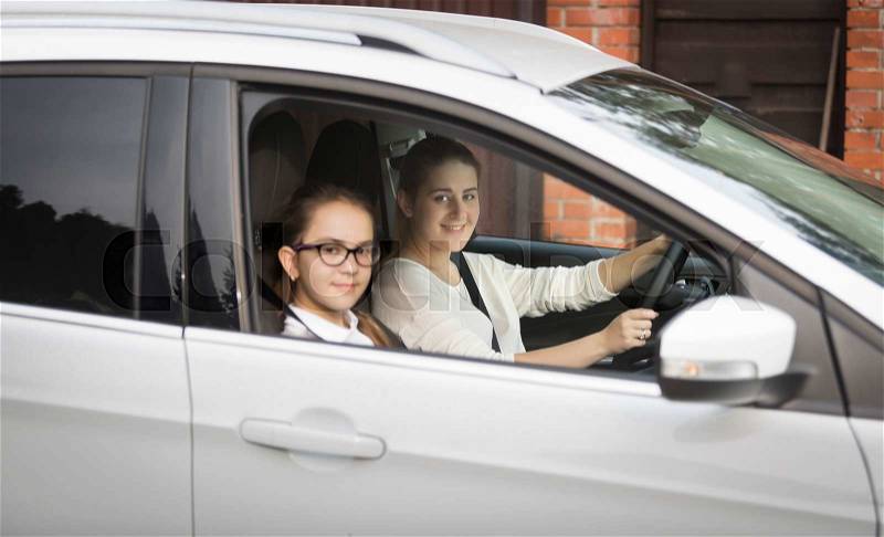 Portrait of cute schoolgirl going with mother to school by car, stock photo