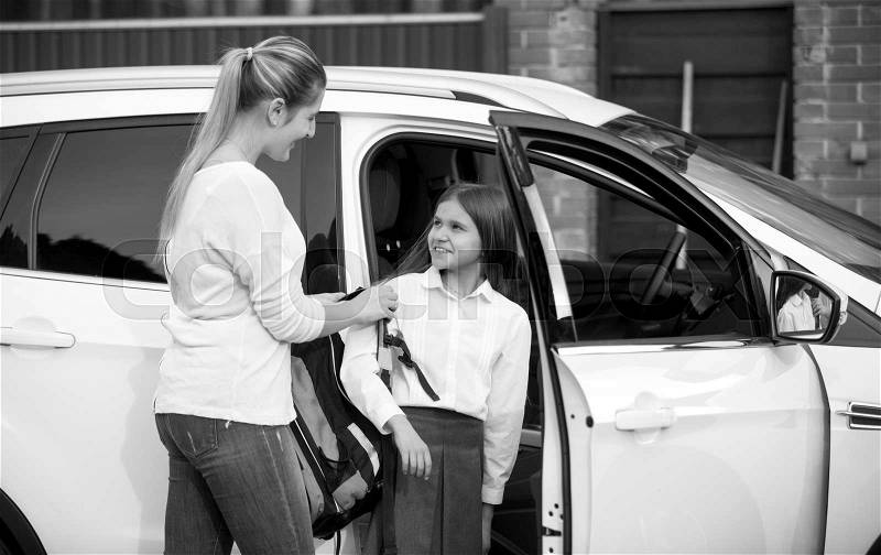 Black and white portrait of schoolgirl getting into the car and giving bag to mother, stock photo