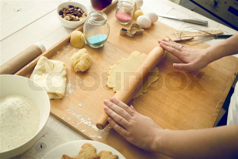Toned photo of young woman rolling dough on wooden board, stock photo