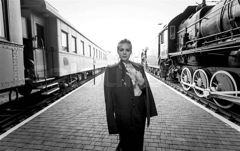 Black and white portrait of young woman in uniform on railroad platform, stock photo