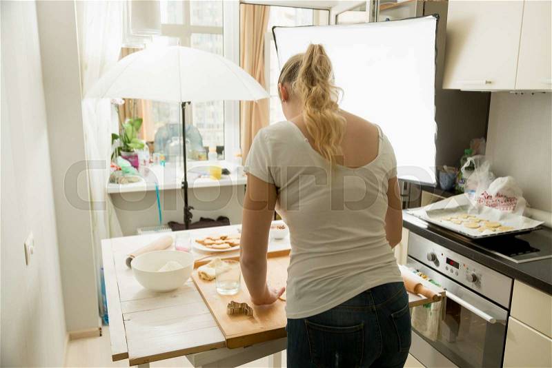 Rear view of woman preparing food for culinary blog. Photography equipment standing on kitchen, stock photo