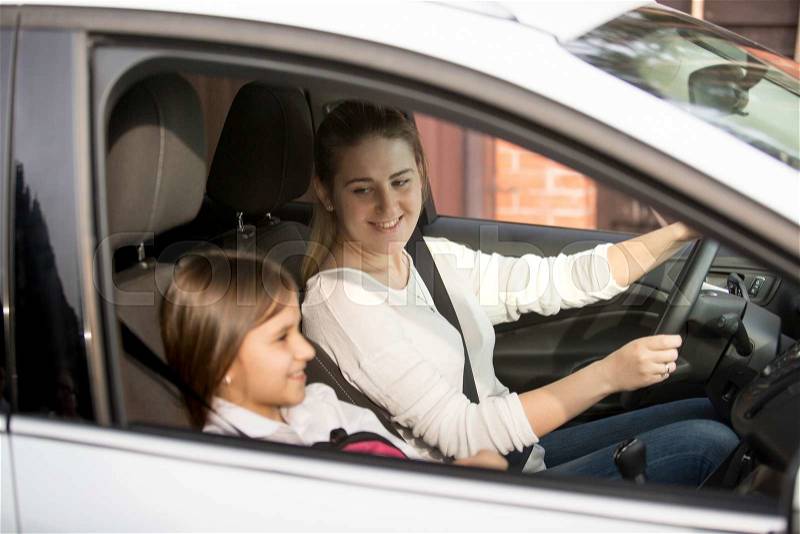 Portrait of young mother driving car to school with daughter, stock photo