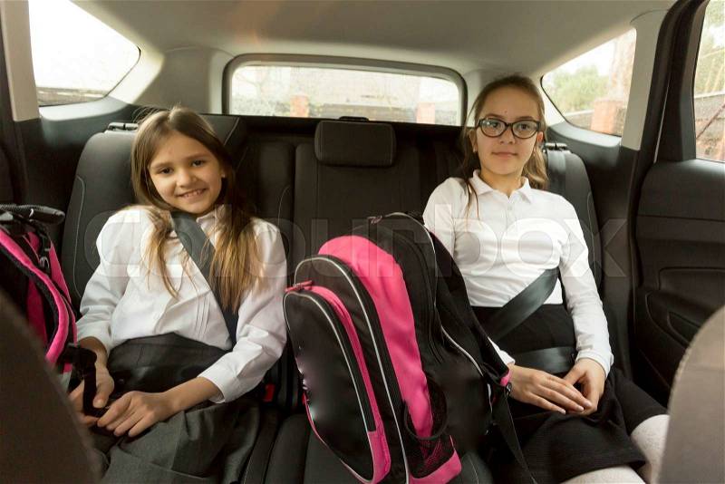 Portrait of two cheerful schoolgirls sitting on car back seat, stock photo