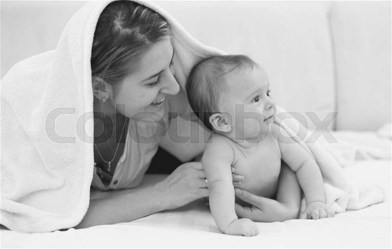 Black and white portrait of happy young mother lying with her 6 month son on bed, stock photo