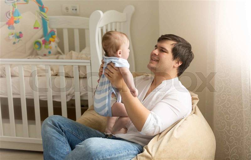 Portrait of happy young man playing with his baby at bedroom, stock photo