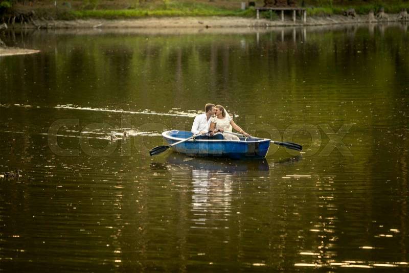 Beautiful newly married couple kissing on rowing boat in the middle of lake, stock photo