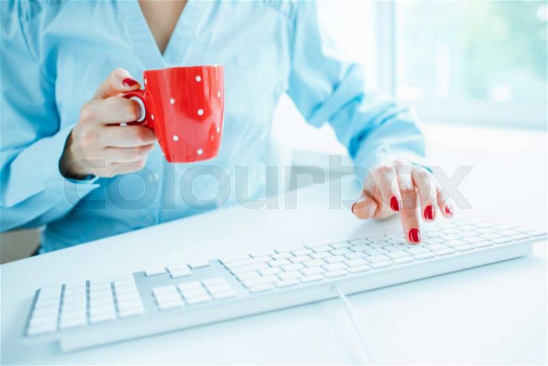 Female hands or woman office worker typing on the keyboard and drinking coffee, stock photo