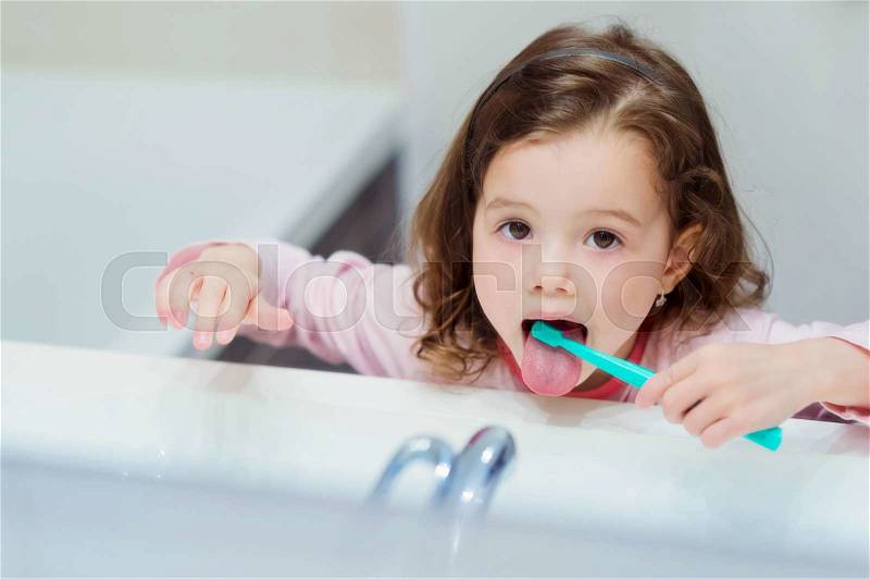 Cute little girl in pink pyjamas in bathroom brushing her teeth, stock photo