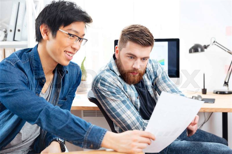Two handsome pensive buinessmen sitting and working with documents in office, stock photo